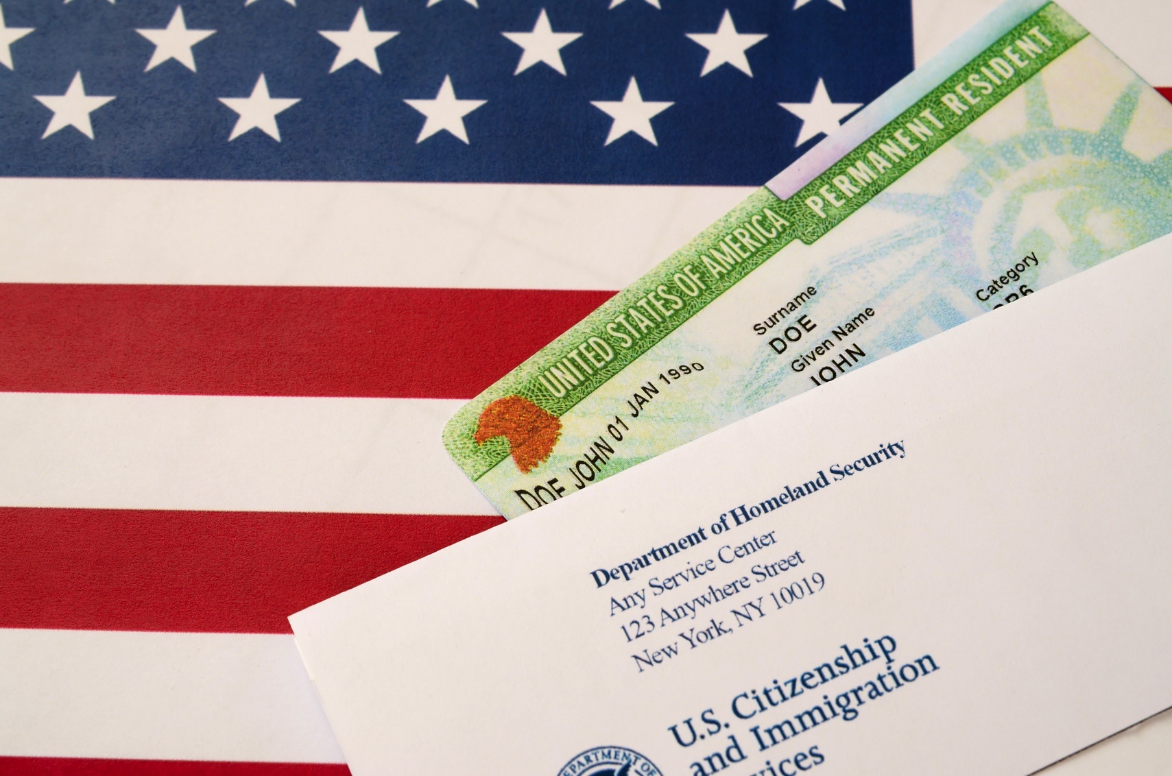 United States Permanent resident green card from dv-lottery lies on United States flag with envelope from Department of Homeland Security close up