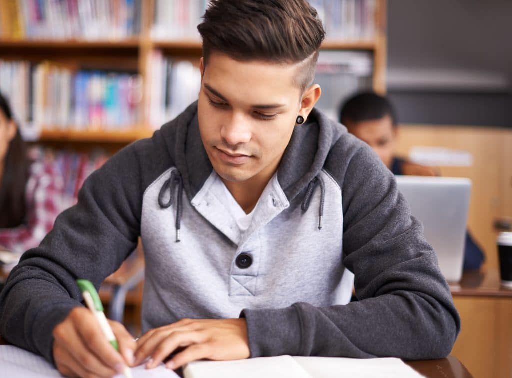 Young man taking notes on the SIJS visa bulletin at a library table.